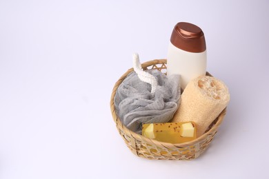 Wicker basket with shower puff, loofah sponge and cosmetic products on white background