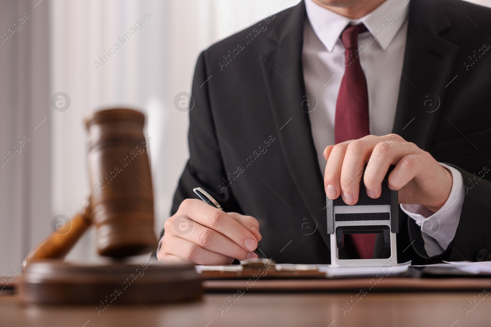 Photo of Notary with pen stamping document at table in office, closeup