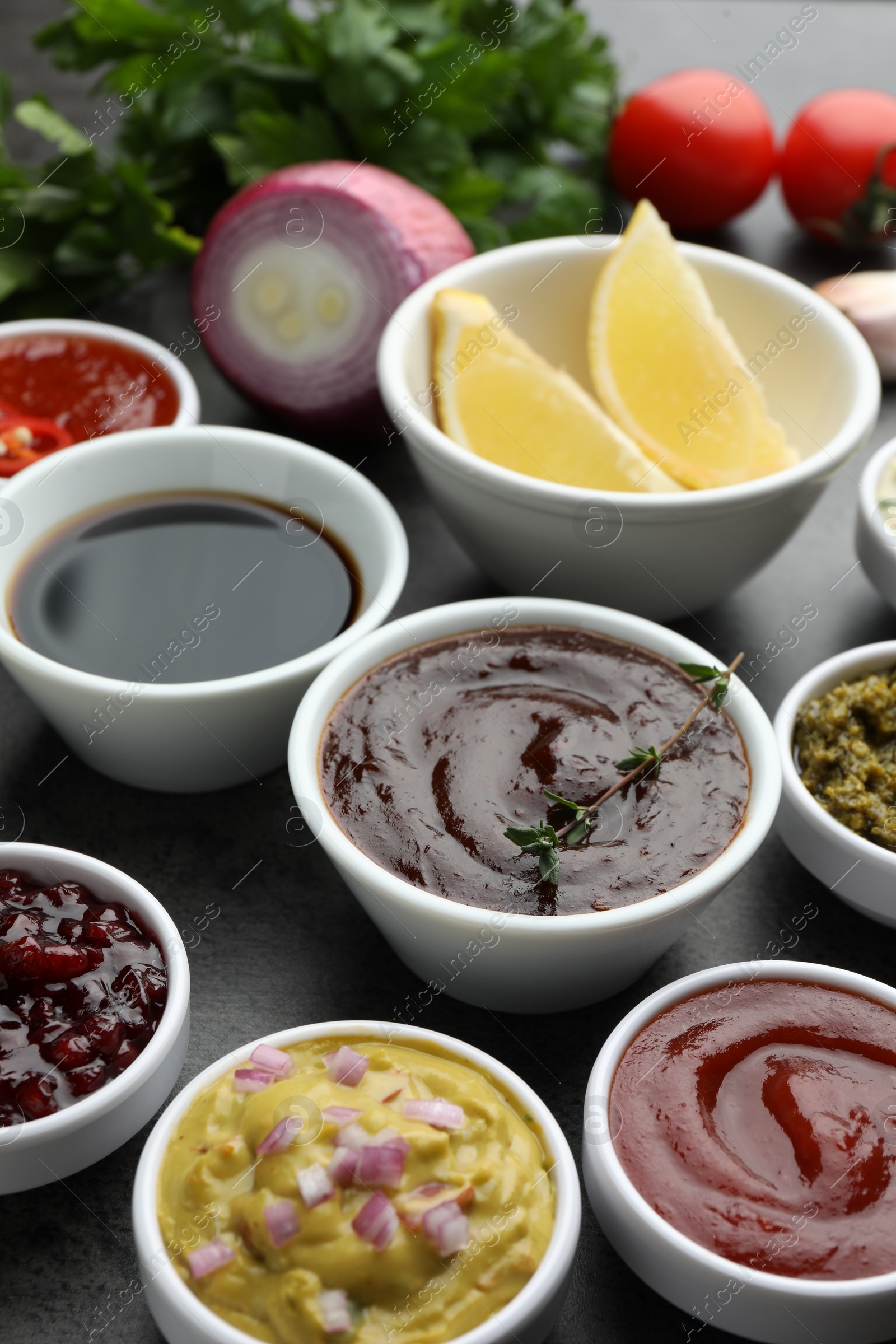 Photo of Different tasty sauces in bowls and ingredients on grey table, closeup