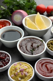 Different tasty sauces in bowls and ingredients on grey table, closeup