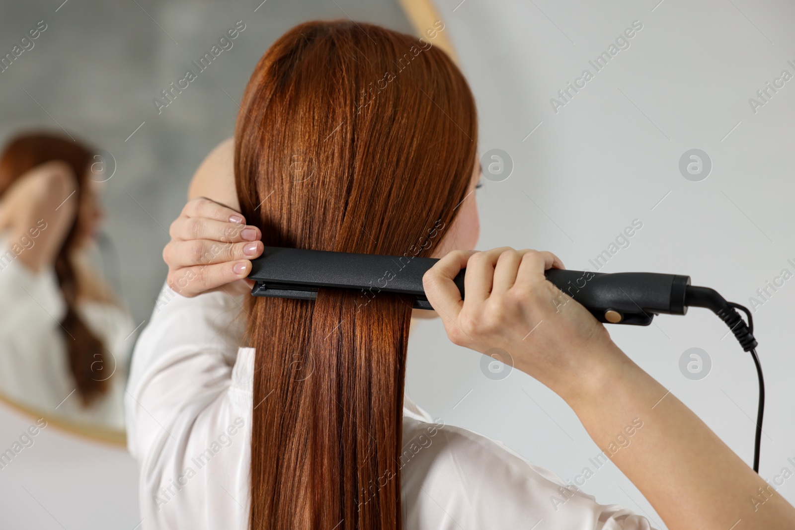 Photo of Beautiful woman using hair iron in room