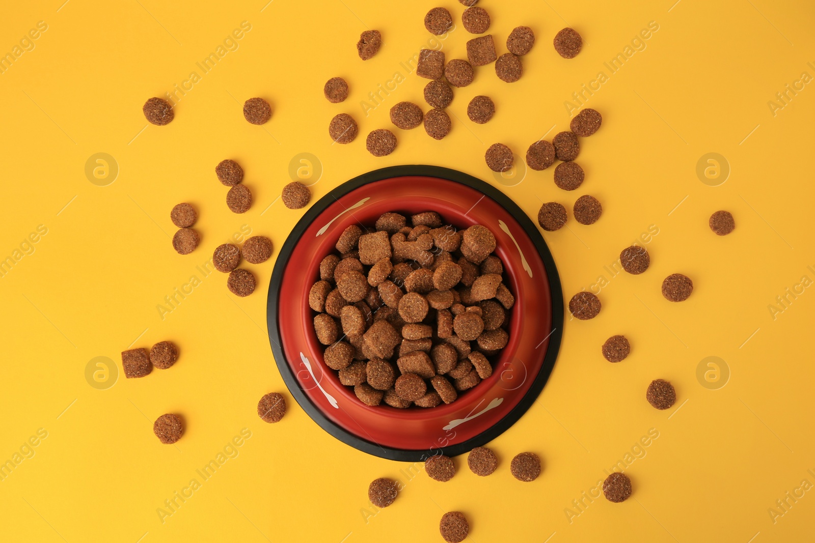 Photo of Dry dog food and feeding bowl on orange background, flat lay