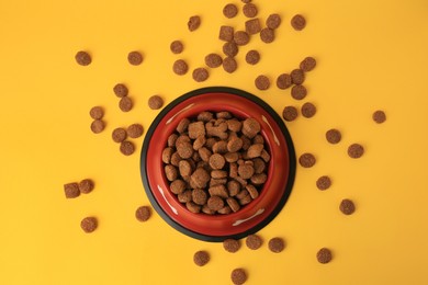 Photo of Dry dog food and feeding bowl on orange background, flat lay