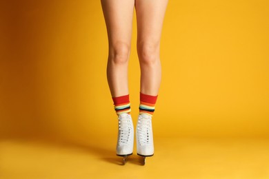 Woman in elegant white ice skates on yellow background, closeup of legs