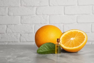 Bottle of essential oil with oranges and leaf on grey marble table against white brick wall. Space for text