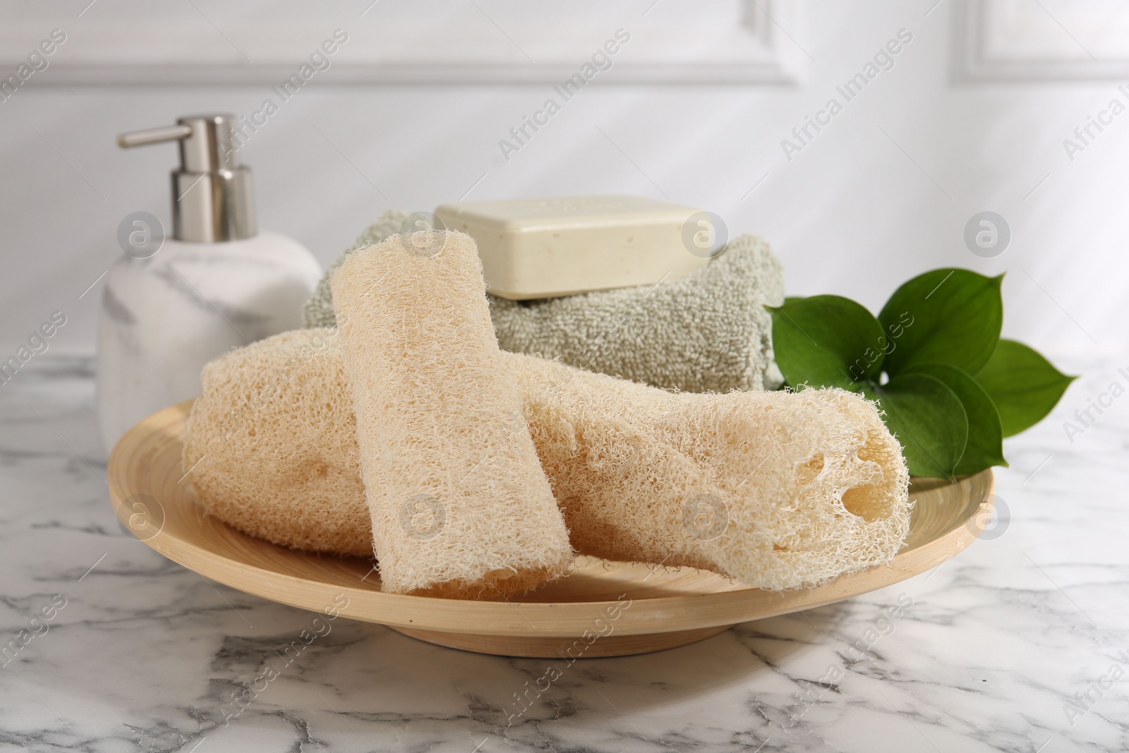 Photo of Loofah sponges, soap, towel and green leaves on white marble table