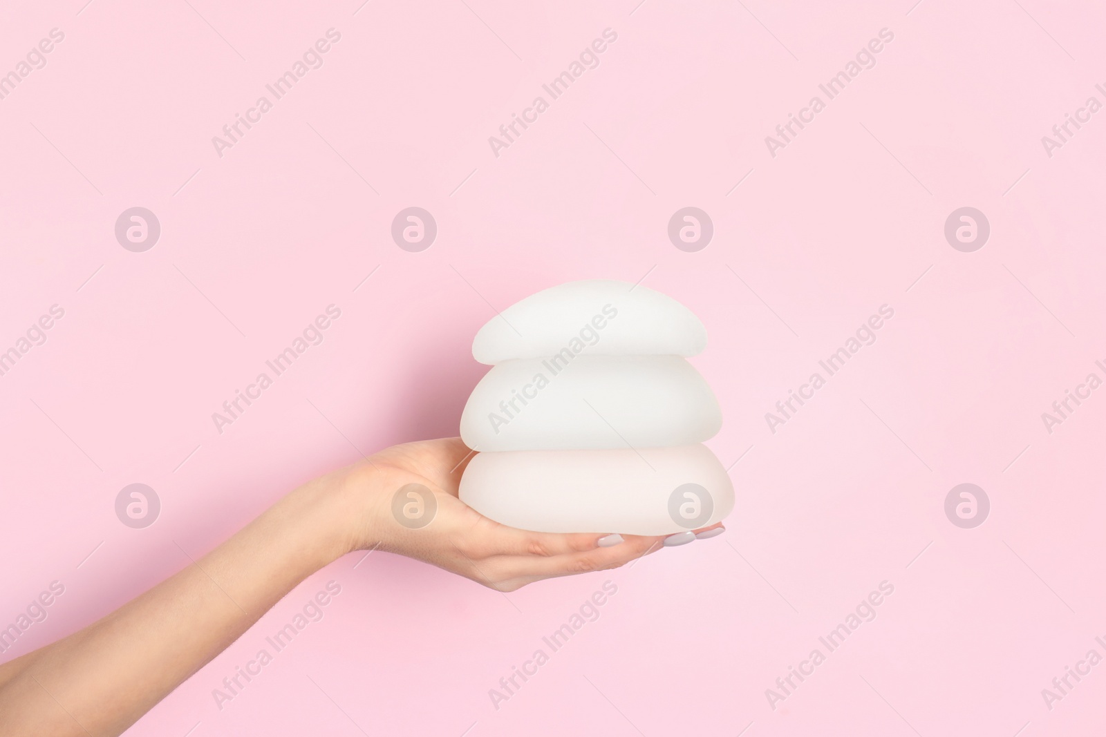 Photo of Woman holding silicone implants for breast augmentation on color background, space for text. Cosmetic surgery