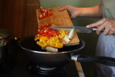 Photo of Woman putting cut vegetables into frying pan in kitchen, closeup