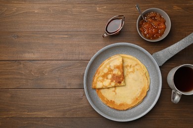 Photo of Frying pan with delicious crepes, jam, syrup and aromatic tea on wooden table, flat lay. Space for text