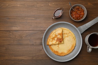 Frying pan with delicious crepes, jam, syrup and aromatic tea on wooden table, flat lay. Space for text