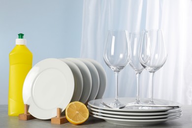 Photo of Glasses, clean dishware and bottle of detergent on grey marble table