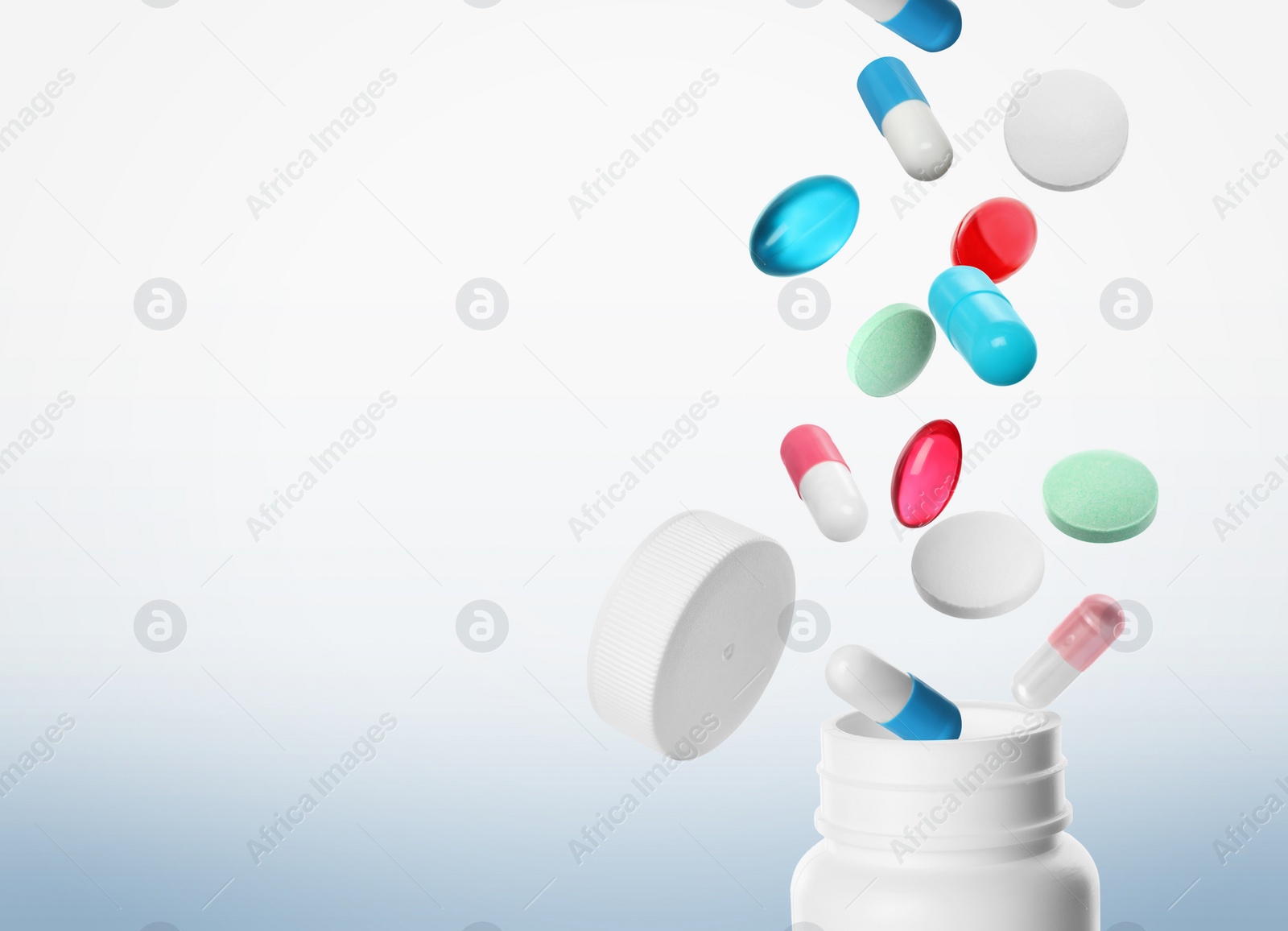 Image of Many different colorful pills falling into bottle on light background