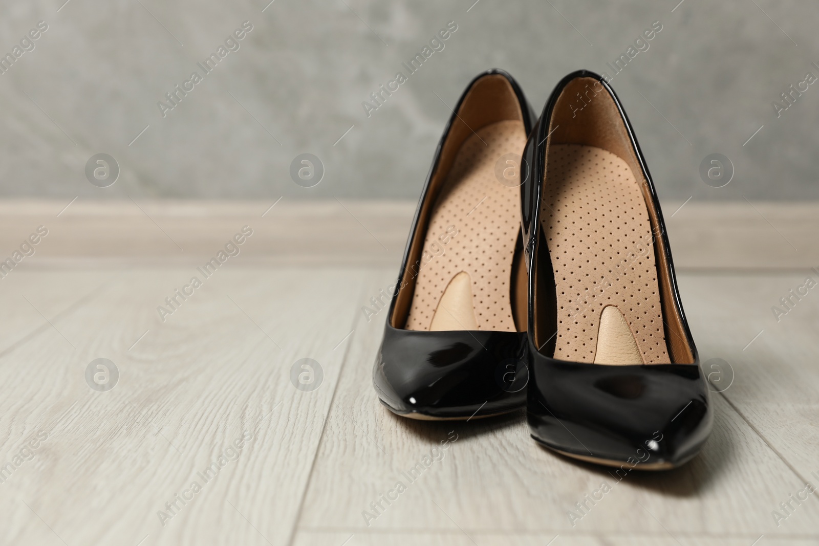 Photo of Orthopedic insoles in high heel shoes on floor, closeup. Space for text