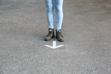 Photo of Woman standing near arrow on asphalt. Choice concept