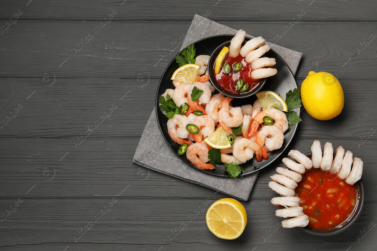 Photo of Tasty boiled shrimps with cocktail sauce, chili, parsley and lemon on grey wooden table, flat lay. Space for text