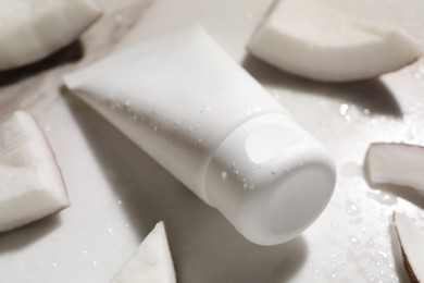 Photo of Tube of hand cream and coconut pieces on wet marble table, closeup