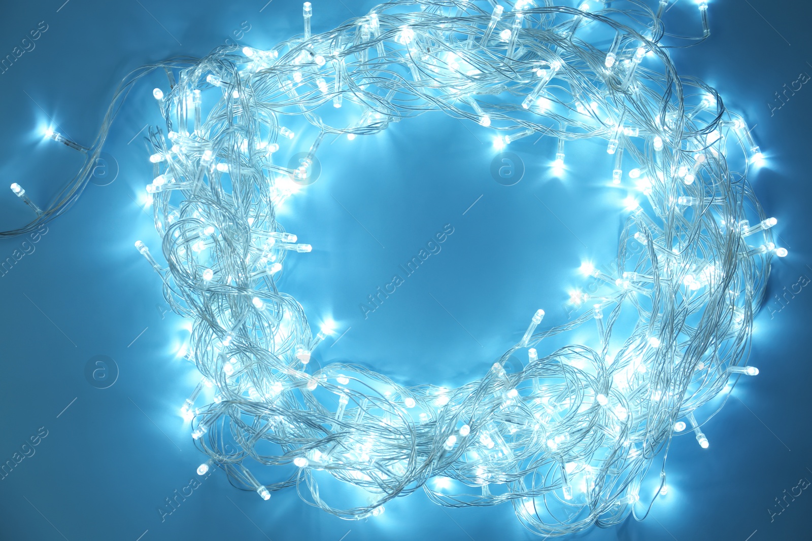 Photo of Frame made of glowing Christmas lights on turquoise background, top view. Space for text