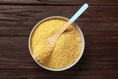 Photo of Millet groats in bowl and spoon on wooden table, top view