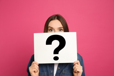 Emotional woman holding question mark sign on pink background