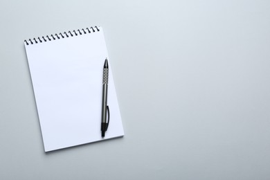 Photo of One notebook and pen on light grey background, top view. Space for text