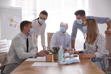 Photo of Group of coworkers with protective masks in office. Business meeting during COVID-19 pandemic
