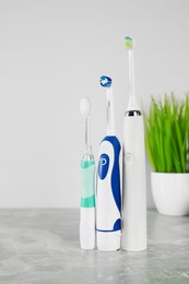 Different electric toothbrushes on light grey marble table near white wall