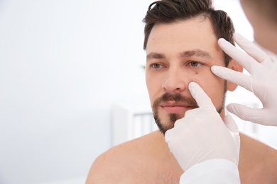 Photo of Dermatologist examining patient's birthmark in clinic. Space for text