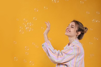Photo of Young woman playing with soap bubbles on yellow background, space for text