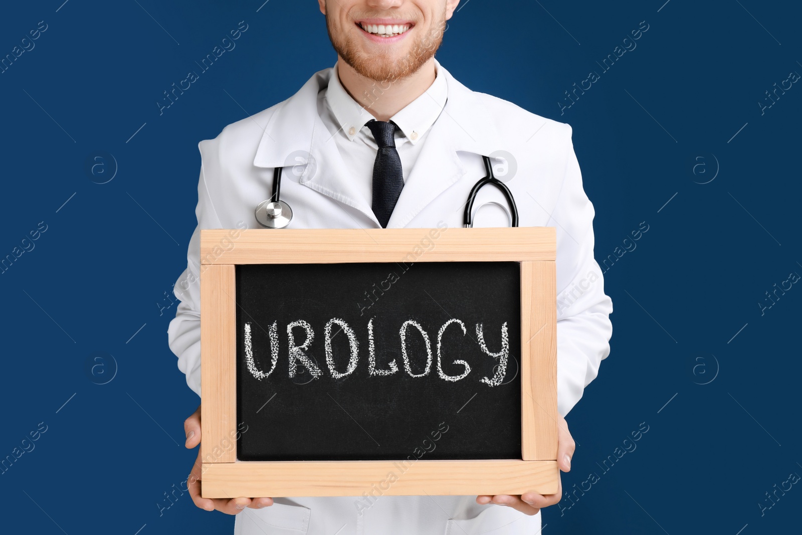 Photo of Male doctor holding small blackboard with word UROLOGY on blue background, closeup