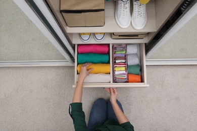 Photo of Woman folding clothes in wardrobe drawer indoors, top view. Vertical storage