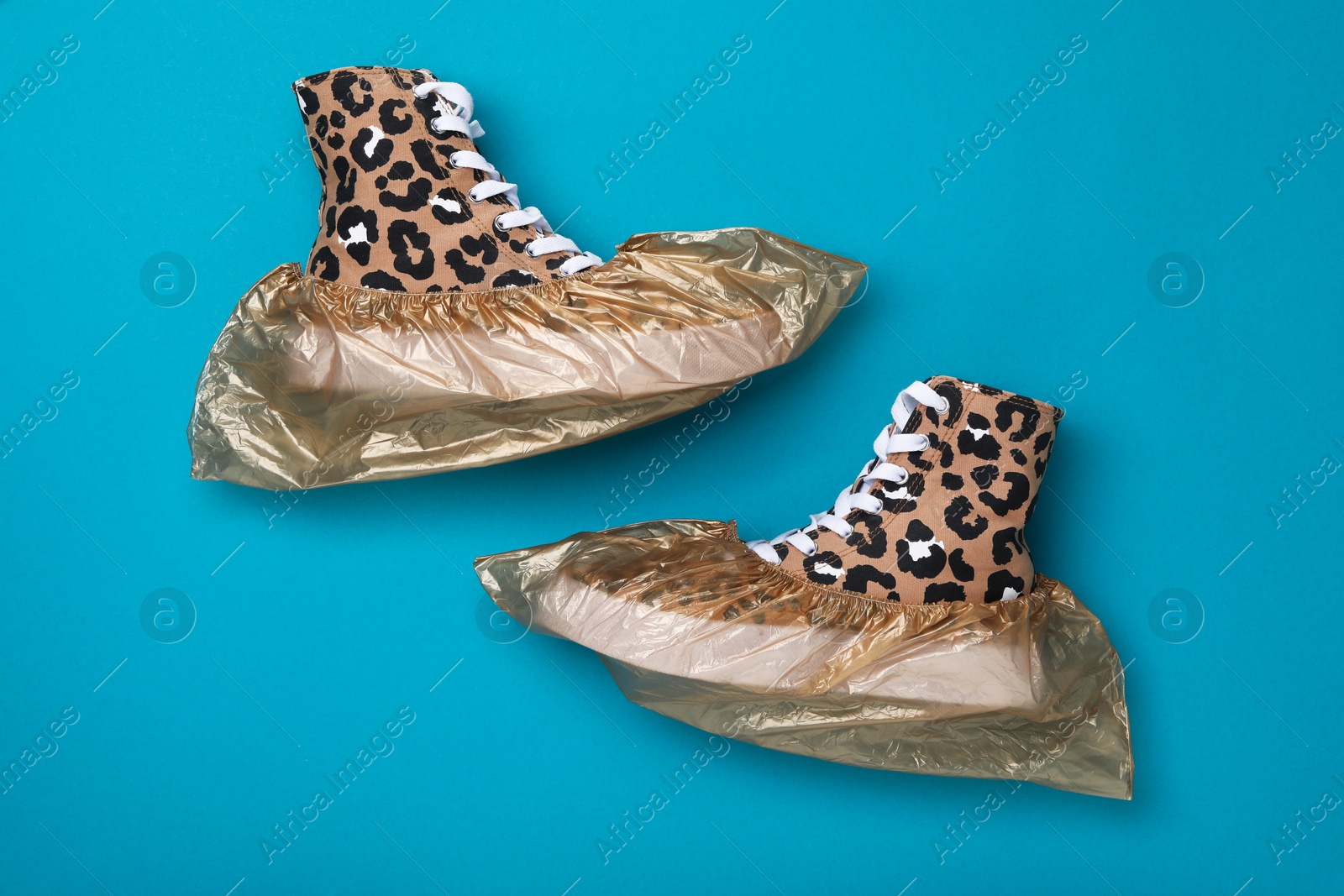 Photo of Sneakers in shoe covers on light blue background, top view