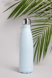 Photo of Stylish thermo bottle near tropical leaves on light grey background