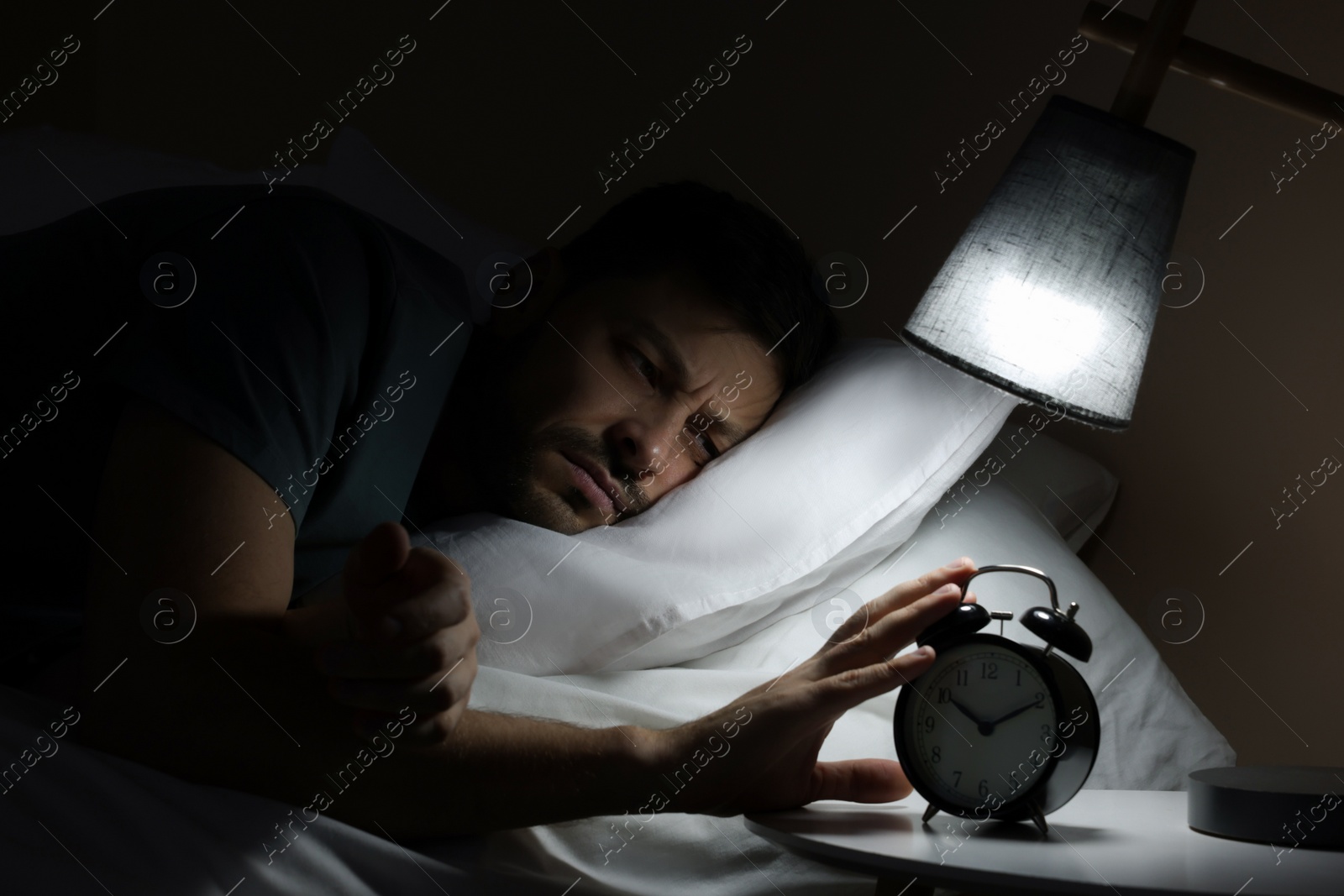 Photo of Sleepy man turning off alarm clock on nightstand in morning