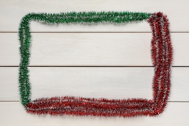 Photo of Frame of bright tinsel on white wooden background, top view. Space for text