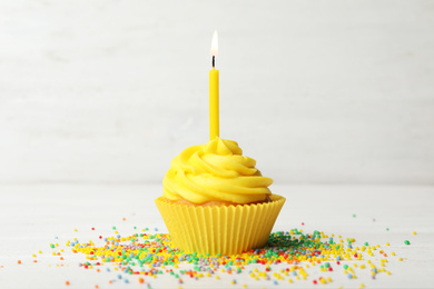 Delicious birthday cupcake with cream and burning candle on white wooden table