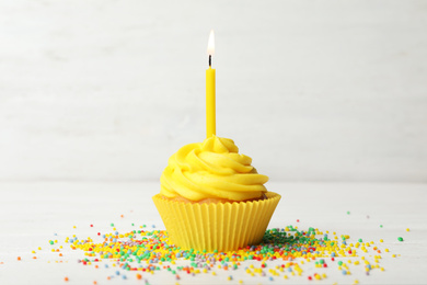 Photo of Delicious birthday cupcake with cream and burning candle on white wooden table