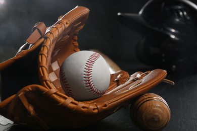Photo of Baseball glove, bat and ball on black table, closeup