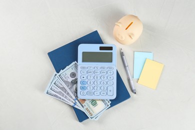 Calculator, dollar banknotes, notebook, pen, sticky notes and piggy bank on light gray table, flat lay. Retirement concept