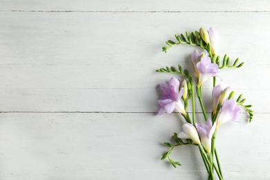 Beautiful fresh freesia flowers on wooden background, top view. Space for text