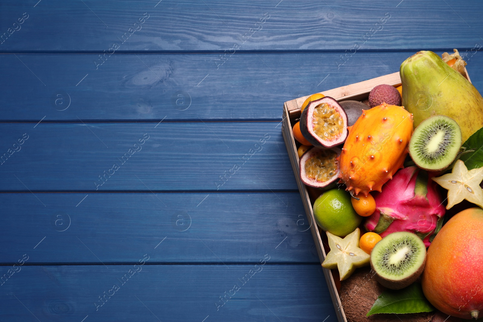 Photo of Crate with different exotic fruits on blue wooden table, top view. Space for text