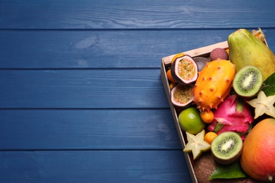 Photo of Crate with different exotic fruits on blue wooden table, top view. Space for text