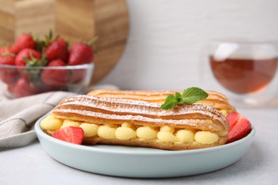 Photo of Delicious eclairs filled with cream, strawberries and mint on light table