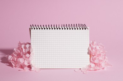 Photo of Beautiful hortensia flowers and notebook on pink background. Space for text