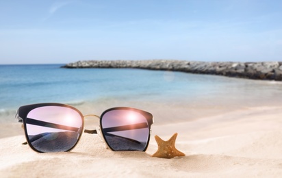 Starfish and stylish sunglasses on sandy beach near sea