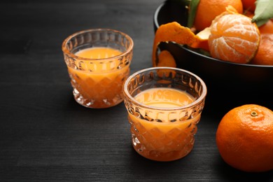 Photo of Tasty tangerine liqueur in glasses and fresh fruits on black wooden table