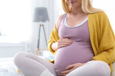 Photo of Pregnant woman sitting on bed in light room, closeup