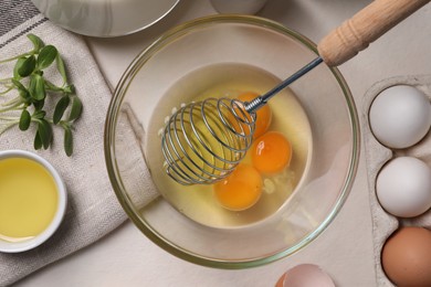 Photo of Flat lay composition with raw eggs and whisk in bowl on light table