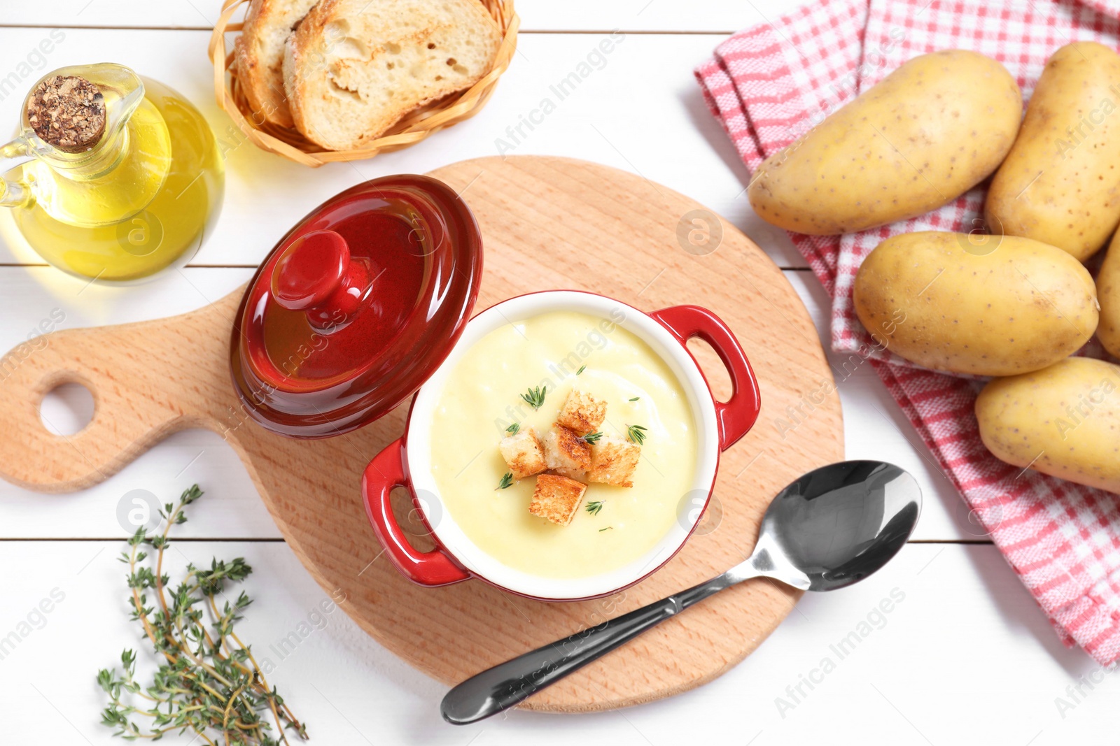 Photo of Tasty potato soup with croutons and rosemary in ceramic pot served on white wooden table, flat lay