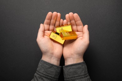Man holding shiny gold bars on black background, top view