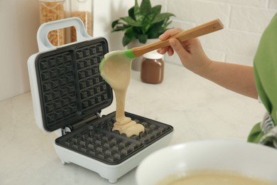 Woman pouring dough onto Belgian waffle maker in kitchen, closeup